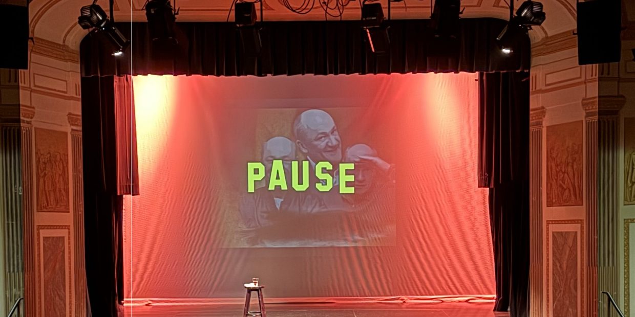 PAUSE Header Bühne in rotem Licht mit Einblendung "Pause" in gelben Großbuchstaben